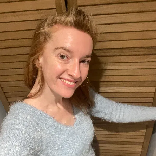 Portrait souriant de Diane de Sagazan, en pull bleu clair devant un mur en bois.